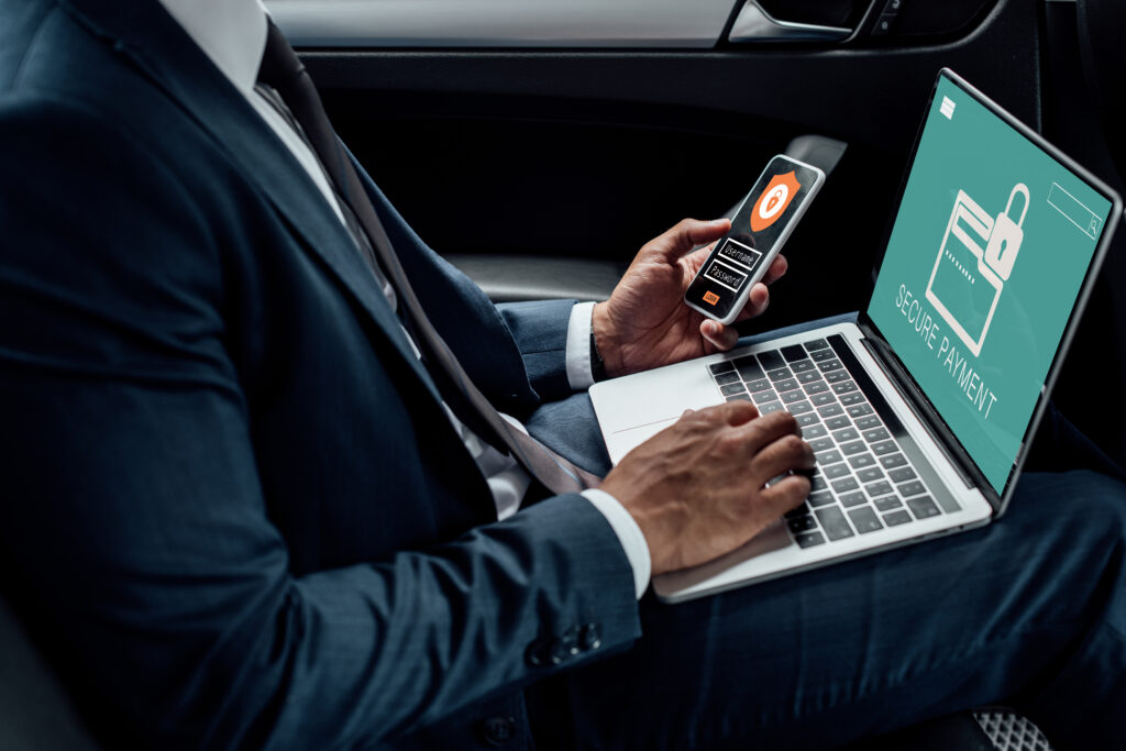 Man in parked car using laptop and cellphone to secure his devices