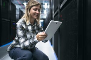Female data center technician working inside server rack room