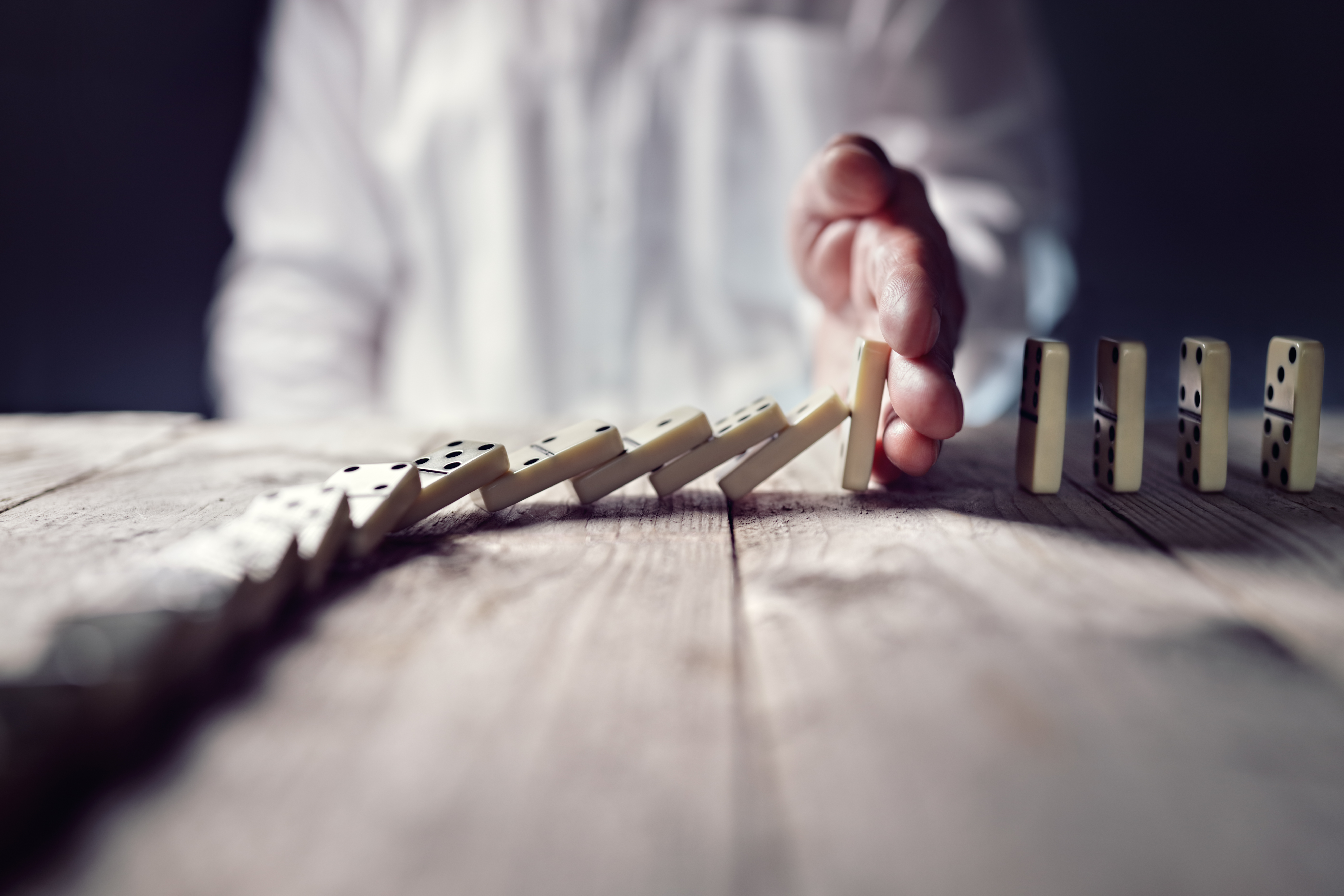 A person stopping a sequence of dominos falling representing an analogy for business to be prepared for anything using business continuity solutions